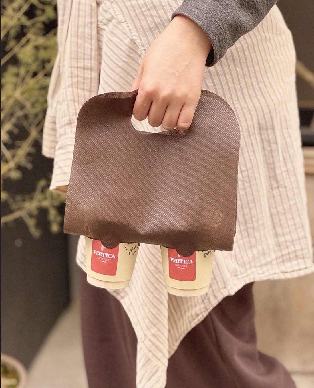 Two Pertica Coffee takeaway cups carried in a brown paper tote on a Nihonbashi street